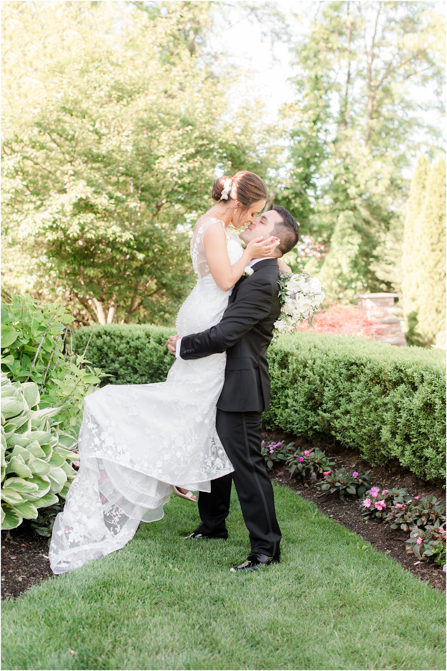 groom lifts bride up in gardens in New Jersey during wedding photos 