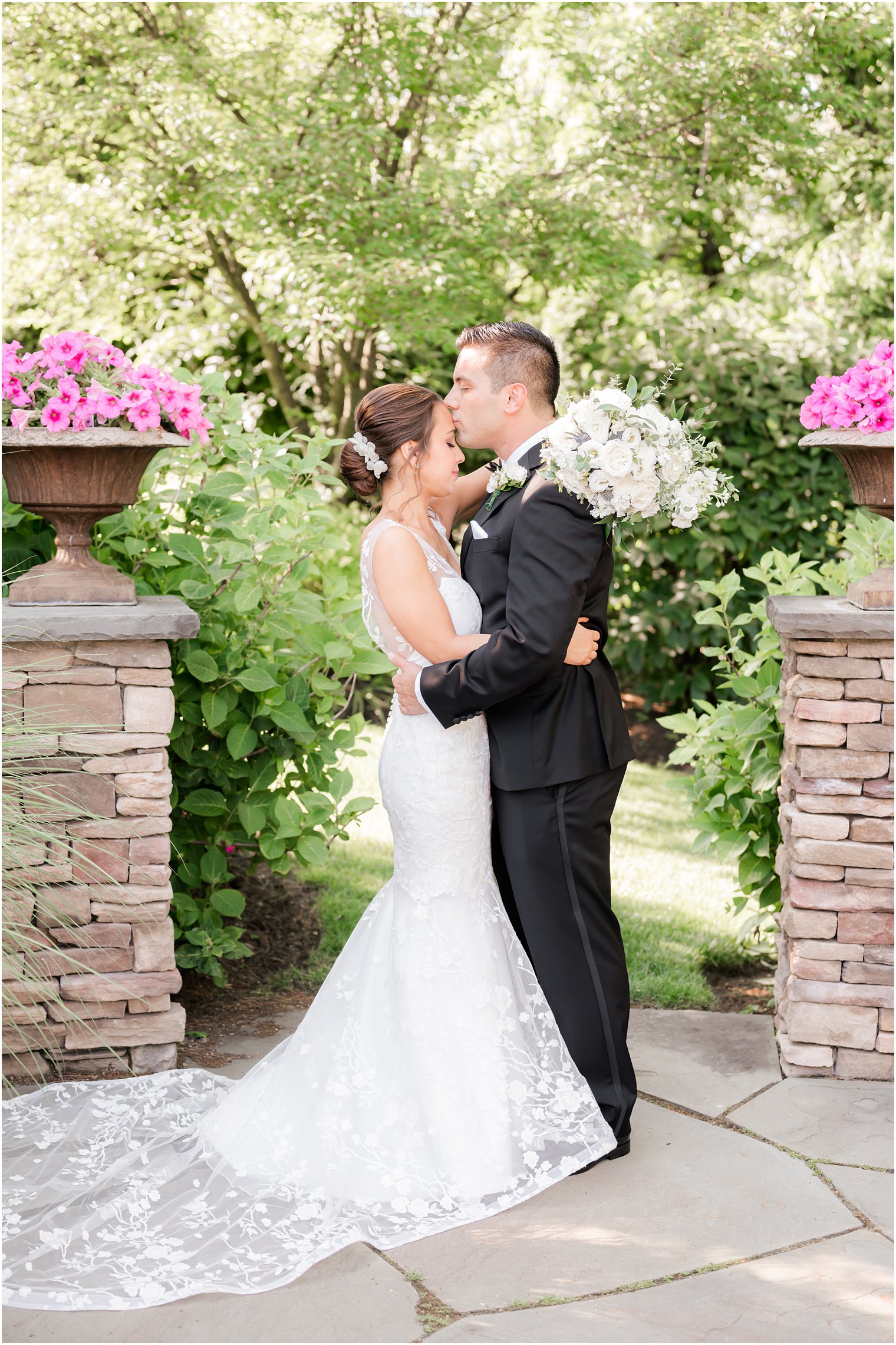 groom kisses bride's forehead with bouquet wrapped around shoulders 