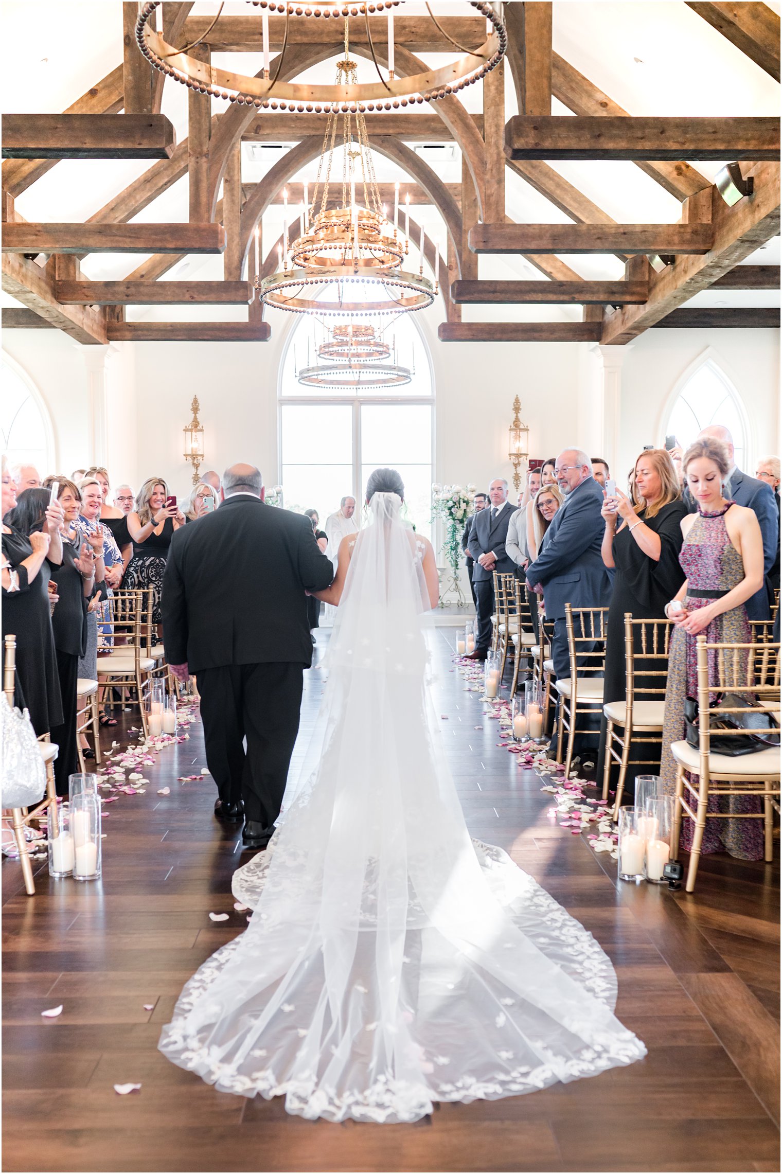 bride walks down aisle with veil dragging behind her 