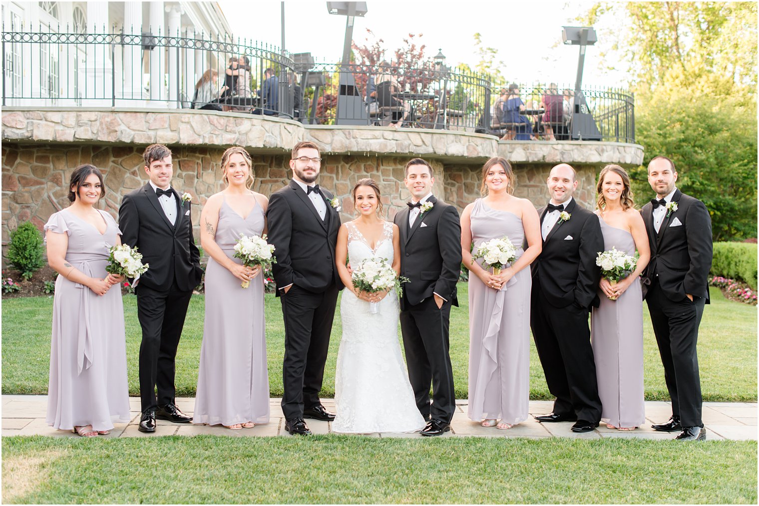 bride and groom pose with bridesmaids in pale purple gowns and groomsmen in suits 