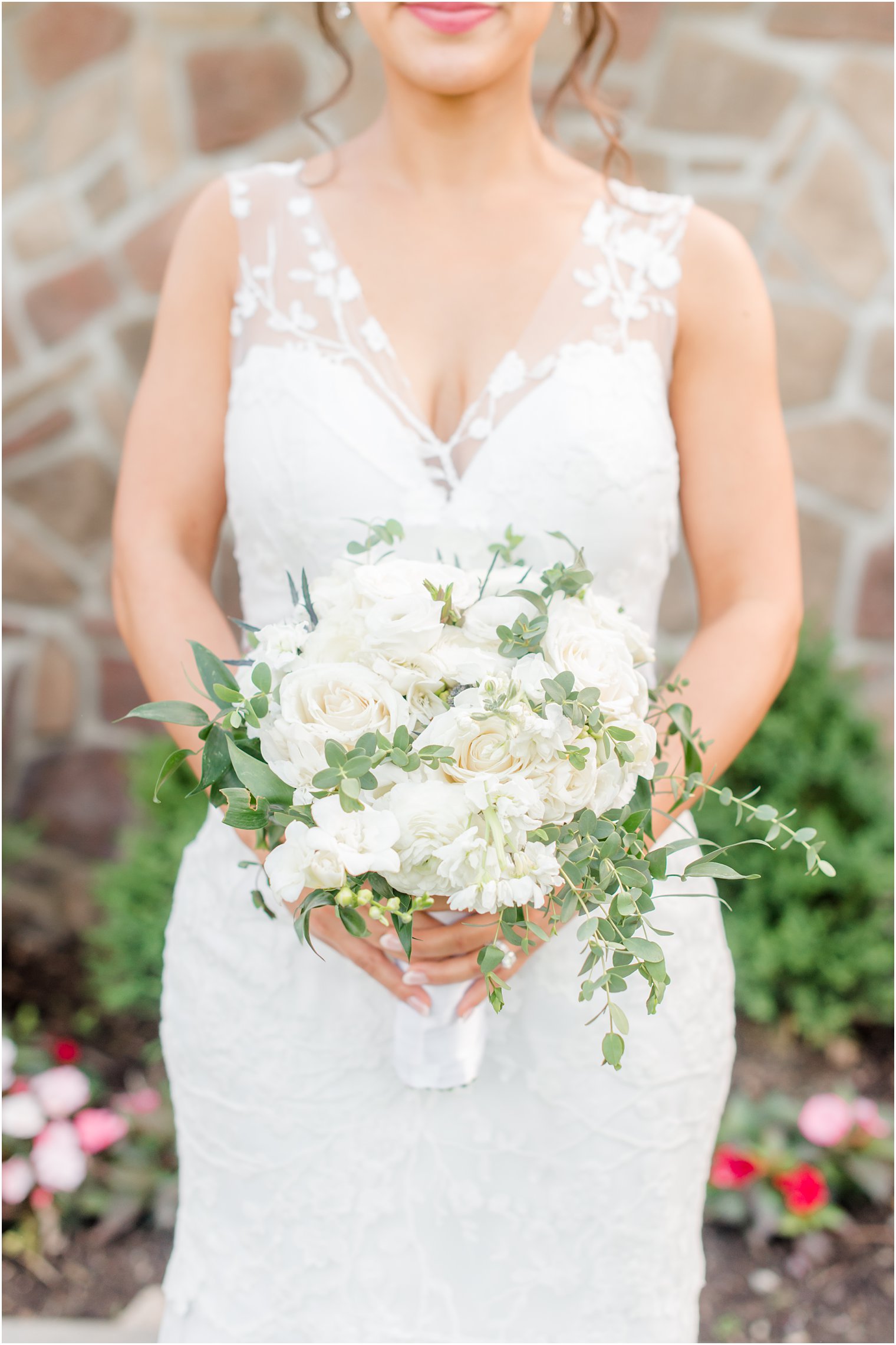 bride holds bouquet of all-white flowers in wedding gown with lace straps 