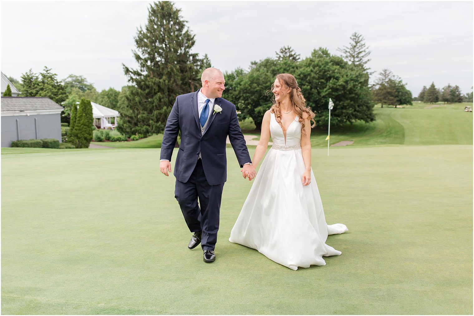 newlyweds hold hands walking on green at Forsgate Country Club
