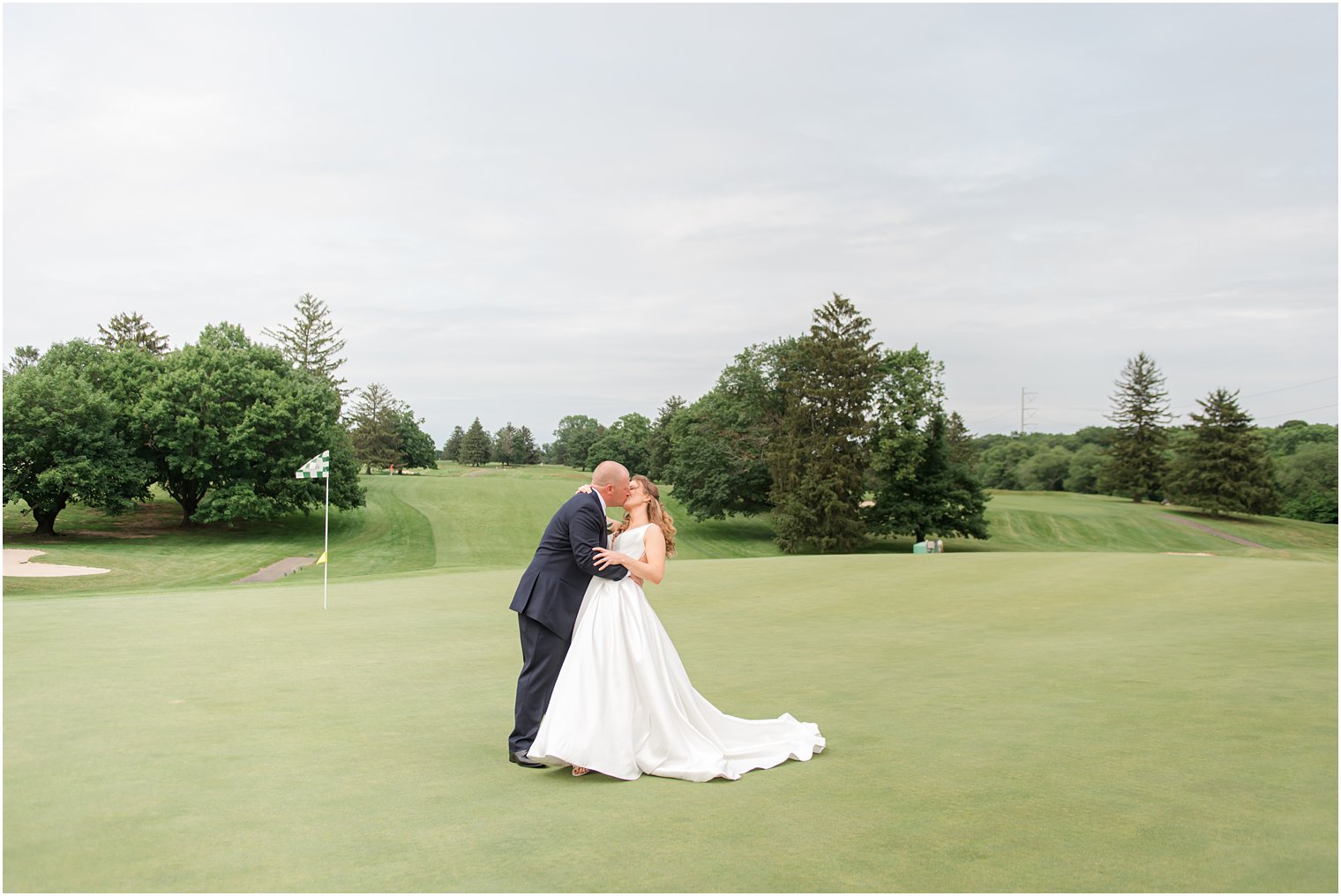 groom kisses bride dipping her on golf course at Forsgate Country Club
