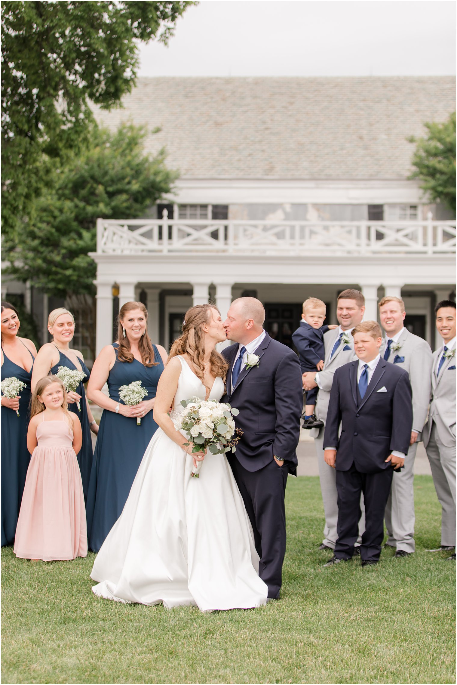 bride and groom kiss with bridal party behind them at Forsgate Country Club