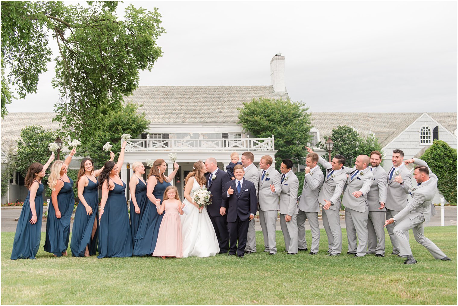 wedding party in navy blue and grey cheers while newlyweds kiss at Forsgate Country Club