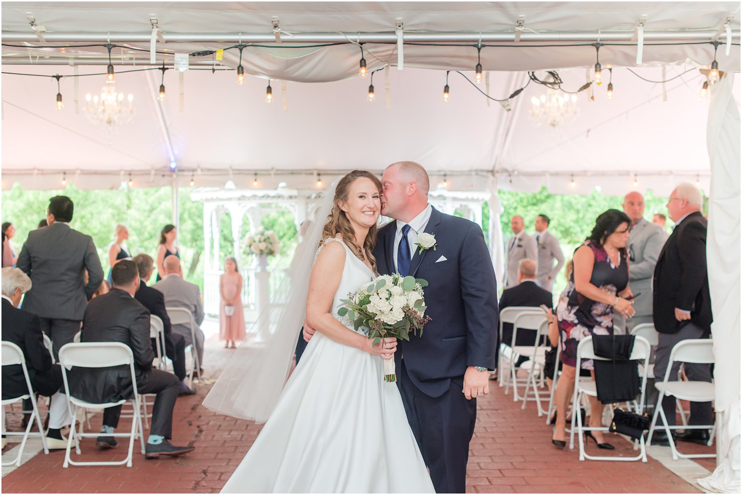 groom kisses bride's cheek at end of aisle at Forsgate Country Club