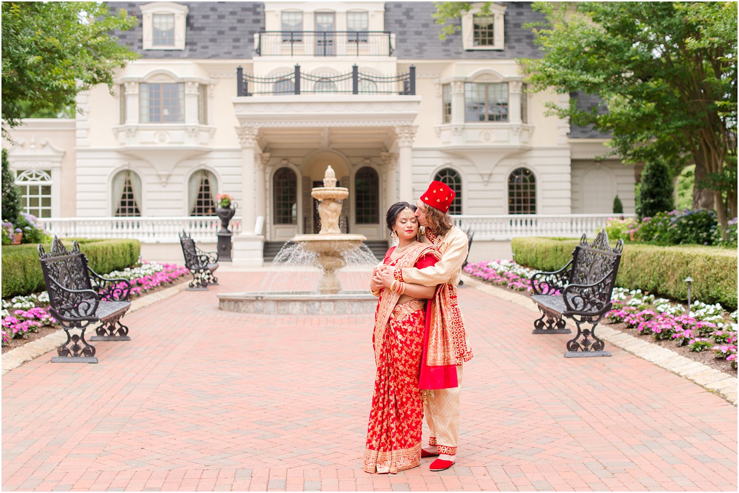 groom hugs bride in front of Ashford Estate in red and gold Indian wedding attire 