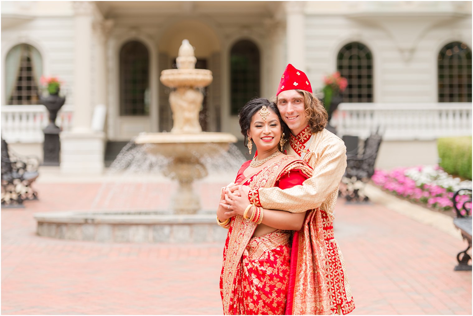 groom hugs bride from behind in red and gold attire for Hindu ceremony 