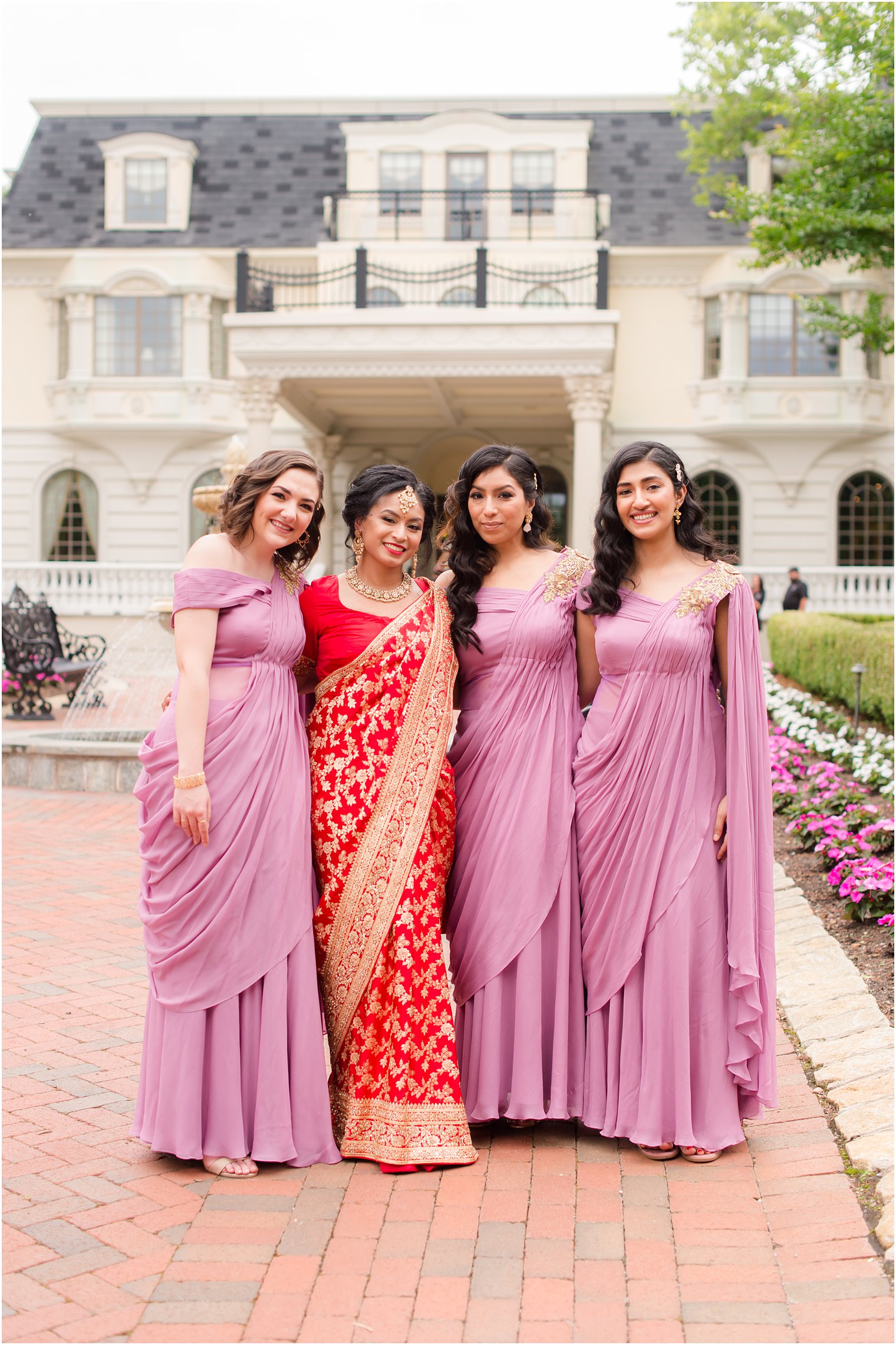 bride in red and gold sari poses with three bridesmaids in pink Hindu dresses 