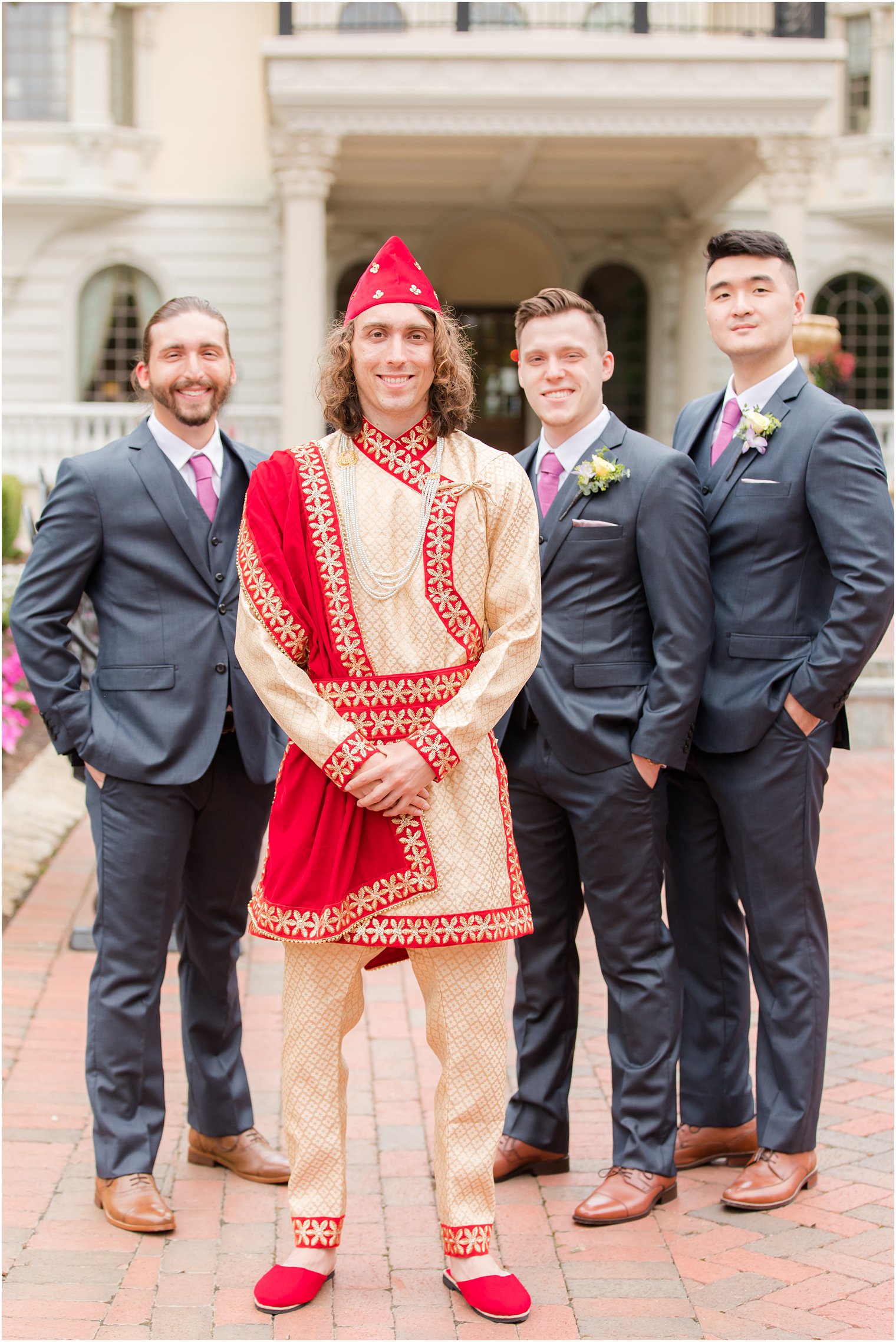 groom in red and gold Hindu attire poses with three groomsmen outside Ashford Estate 