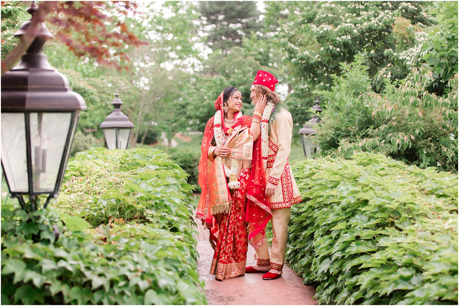 bride and groom pose in gardens of Ashford Estate in traditional red and gold attire for Indian wedding