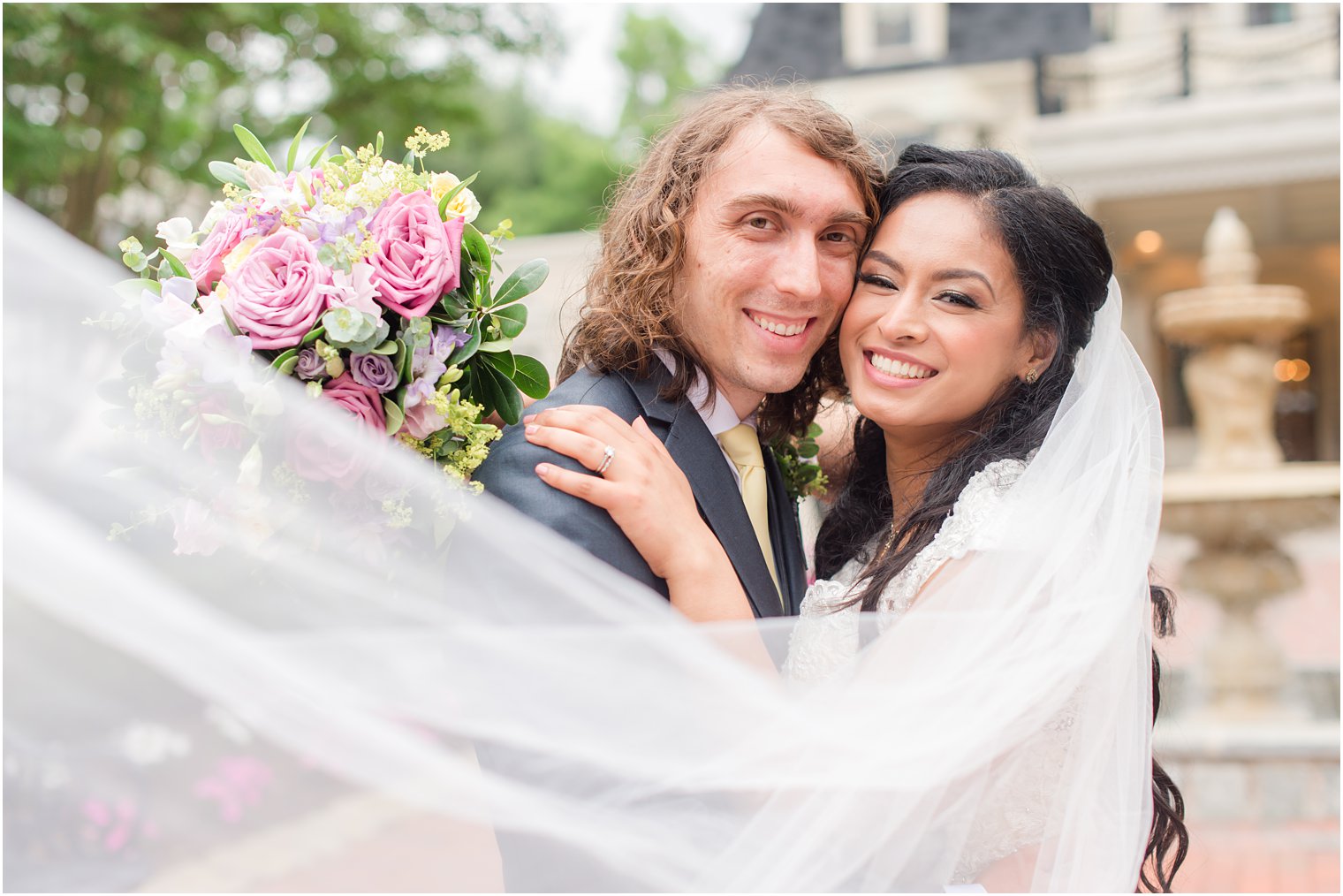 bride and groom hug with cheeks touching with bride's veil draped around them 