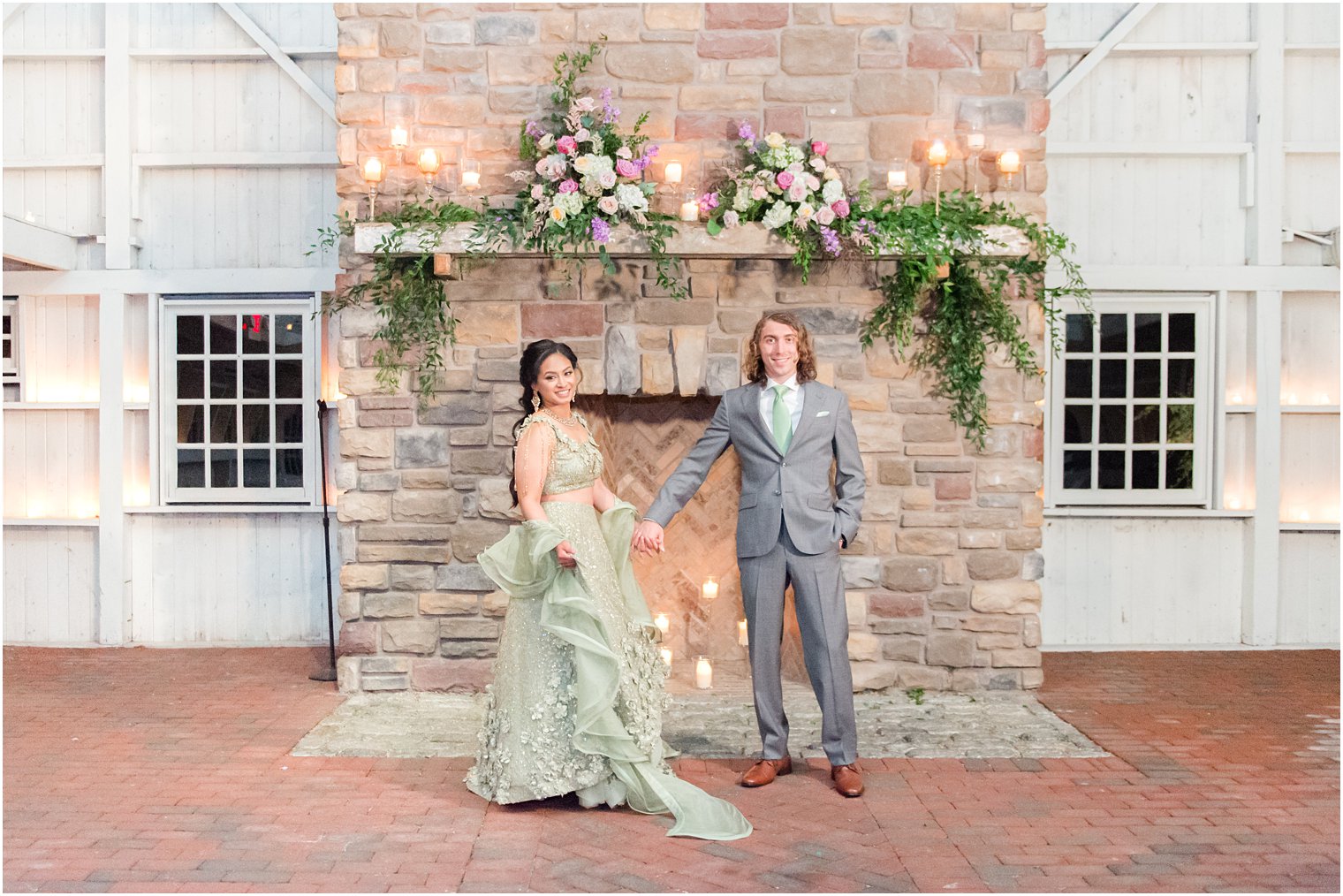 bride and groom pose by fireplace in green sari and grey suit with green tie 