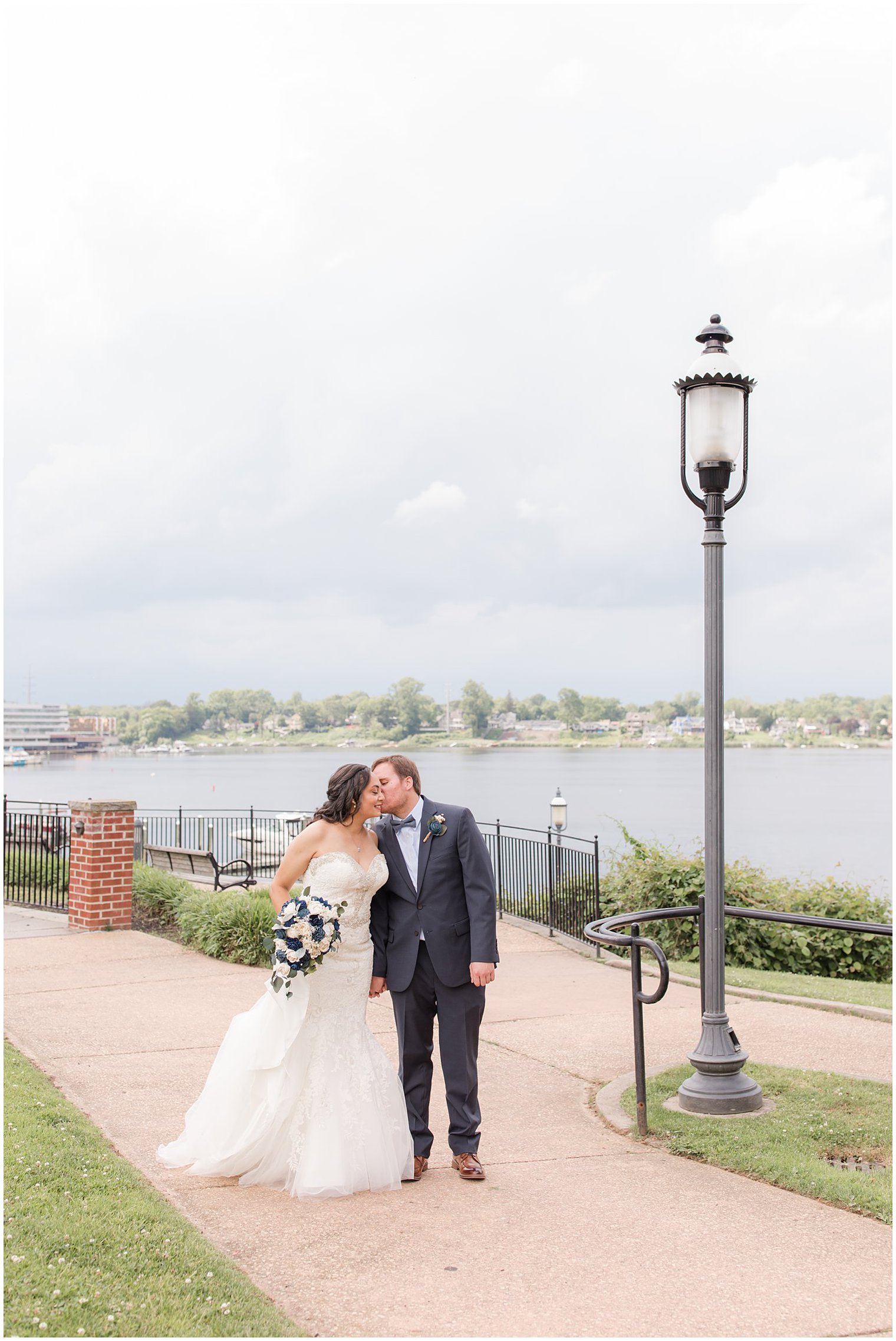 groom kisses bride's cheek during portraits along water in Red Bank