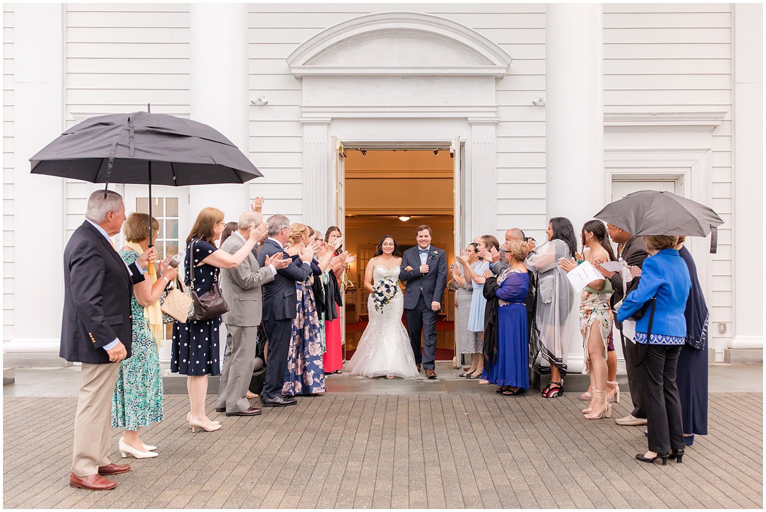 bride and groom leave ceremony with guests under umbrellas 