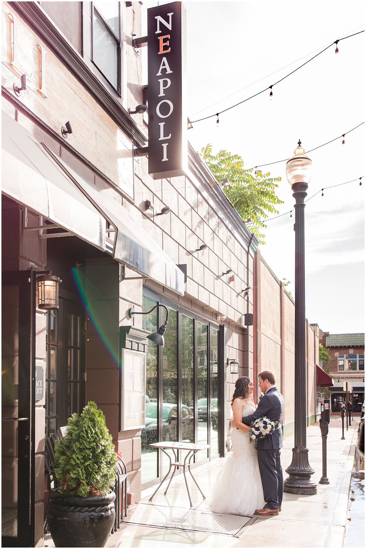 bride and groom hug on street in Red Bank NJ under Neapoli's sign