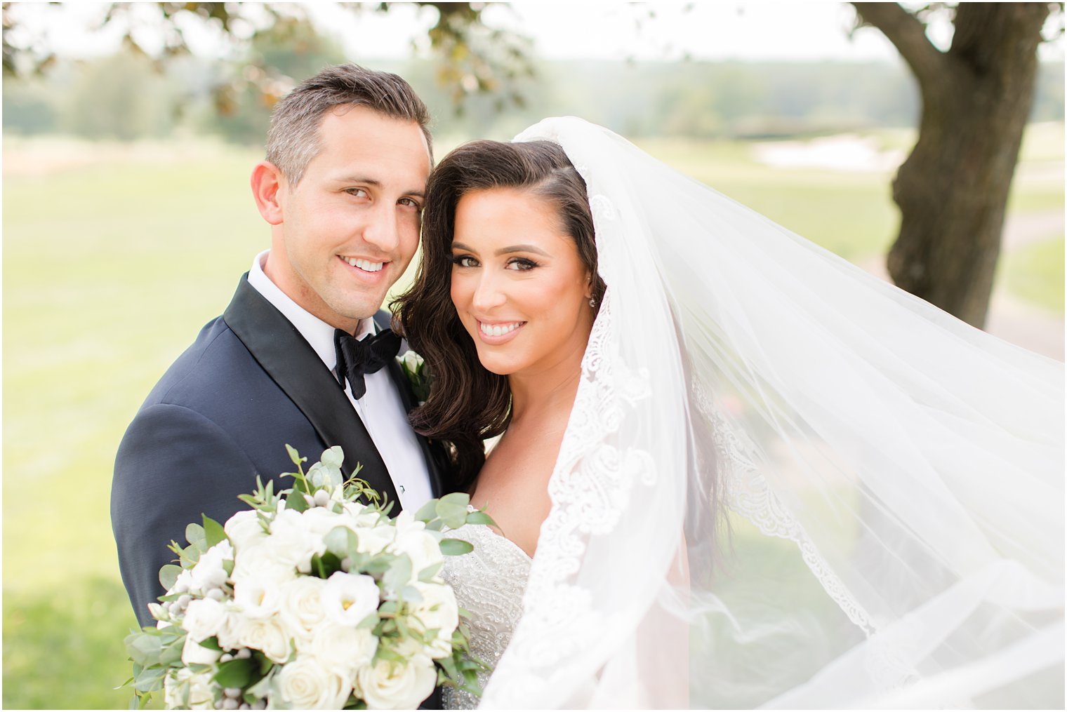 newlyweds lean heads together with bride's veil floating behind her