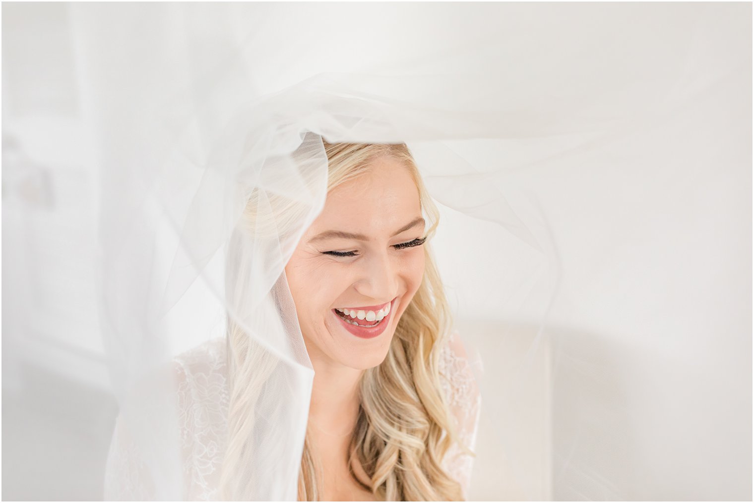 bride laughs under veil during portraits on morning of her wedding 