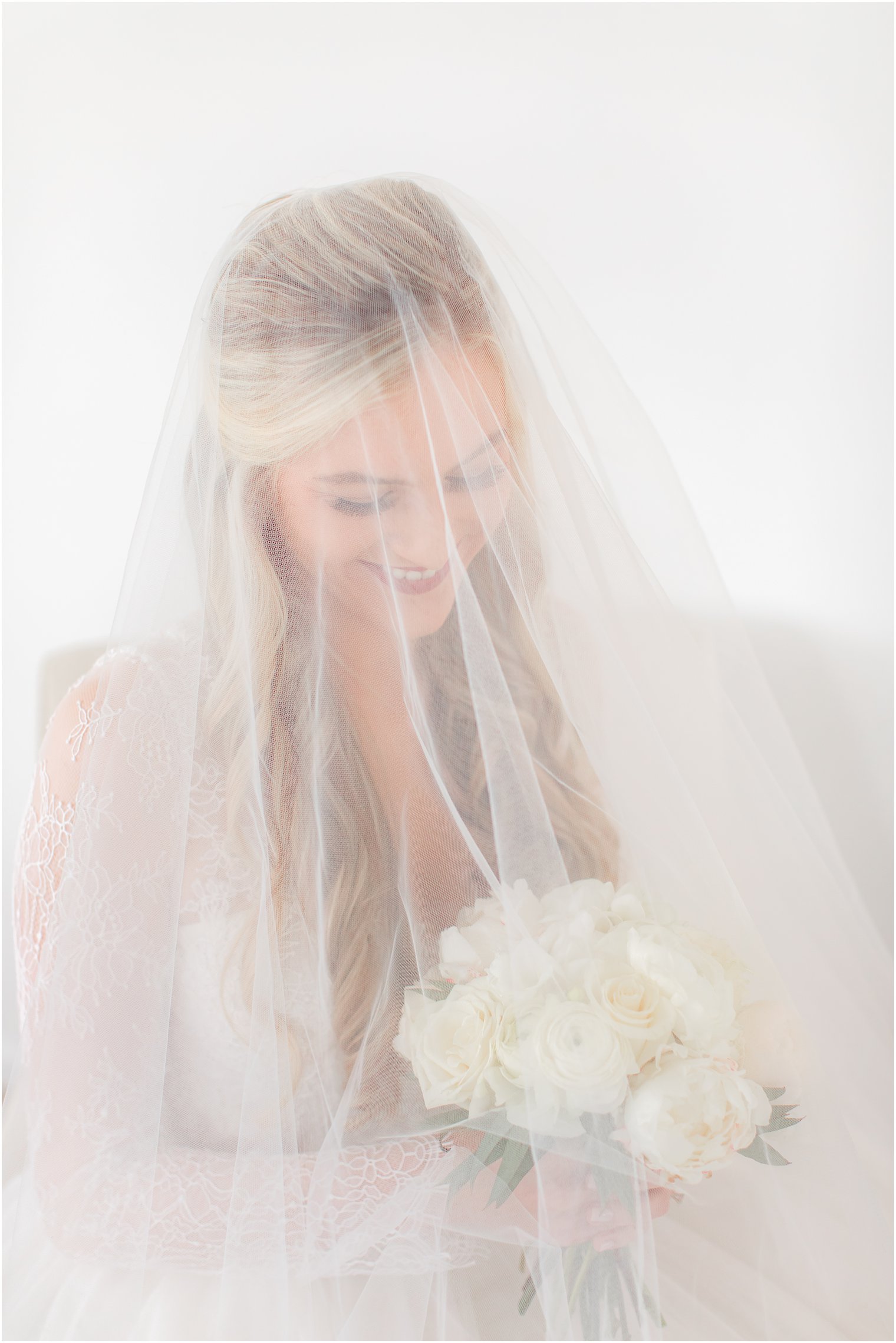 bride looks down at bouquet of ivory flowers under veil before NJ wedding