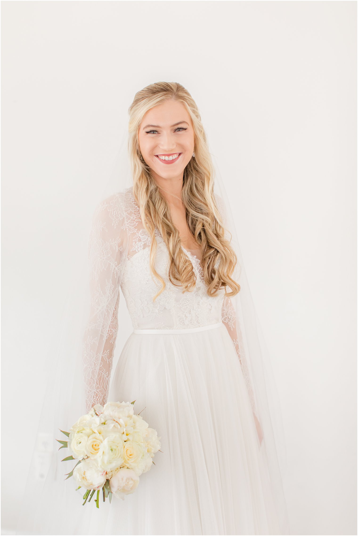 bride in dress with long lace sleeves hold bouquet of ivory roses