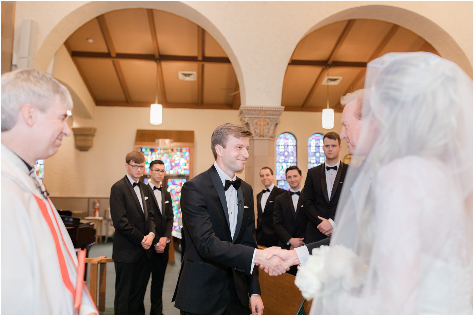 groom shakes father of bride's hand while he gives bride away at traditional church wedding in Ocean City NJ