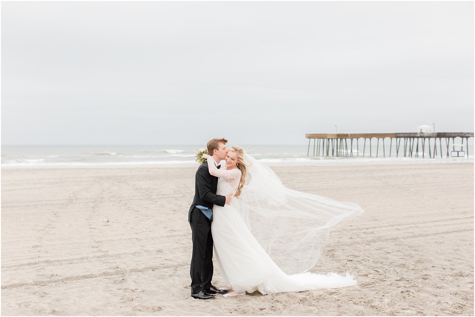 groom kisses bride's cheek during beach wedding photos