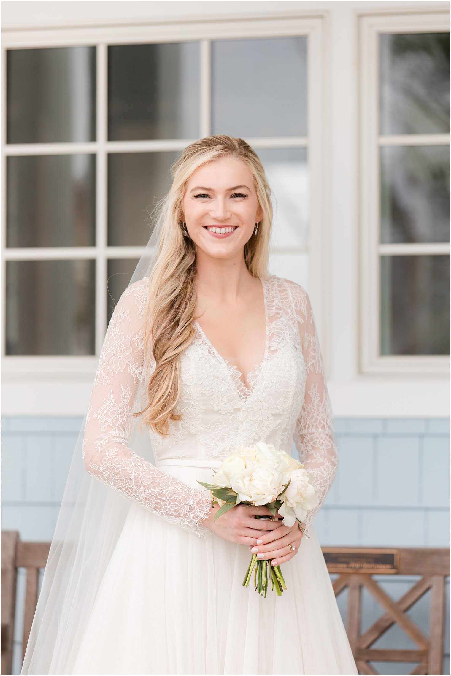 bride in wedding dress with lace sleeves holds small bouquet of white flowers