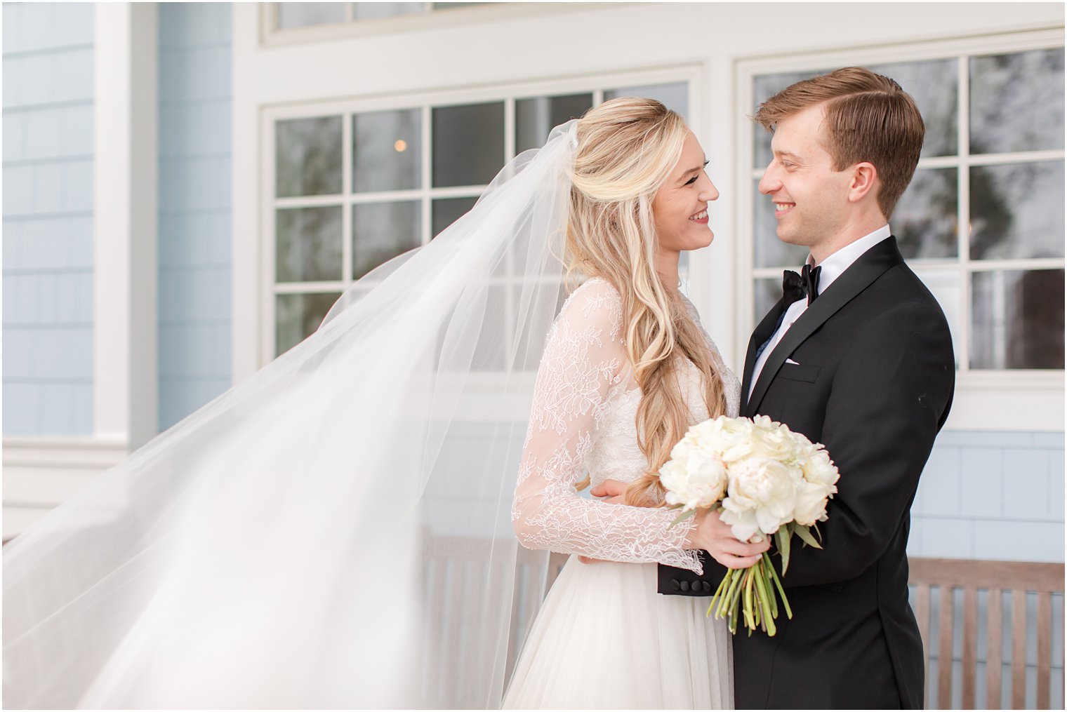 bride and groom smile together with bride's veil floating during Ocean City Yacht Club wedding photos 
