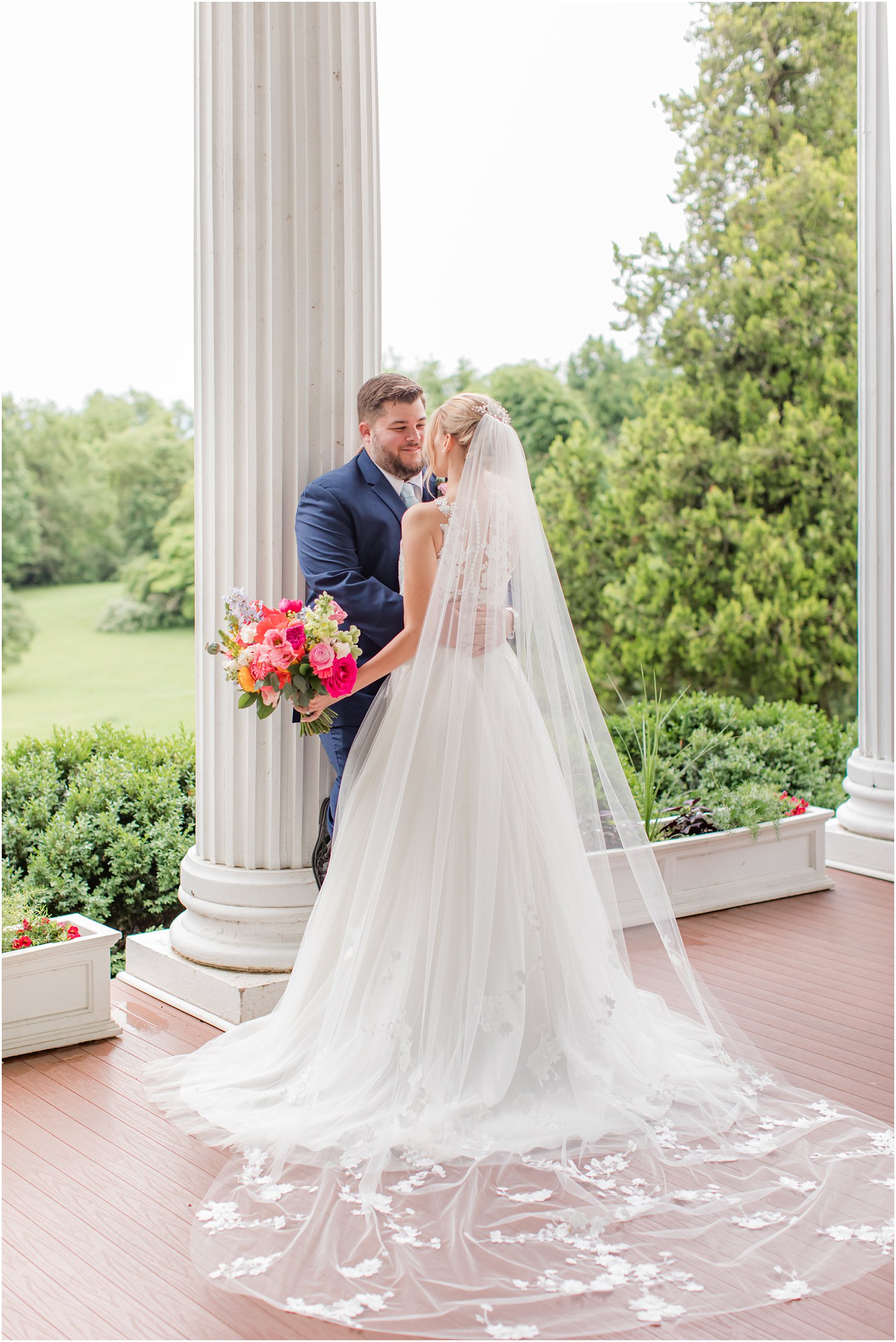 bride and groom hug next to white pillar during spring Rosemont Manor wedding 