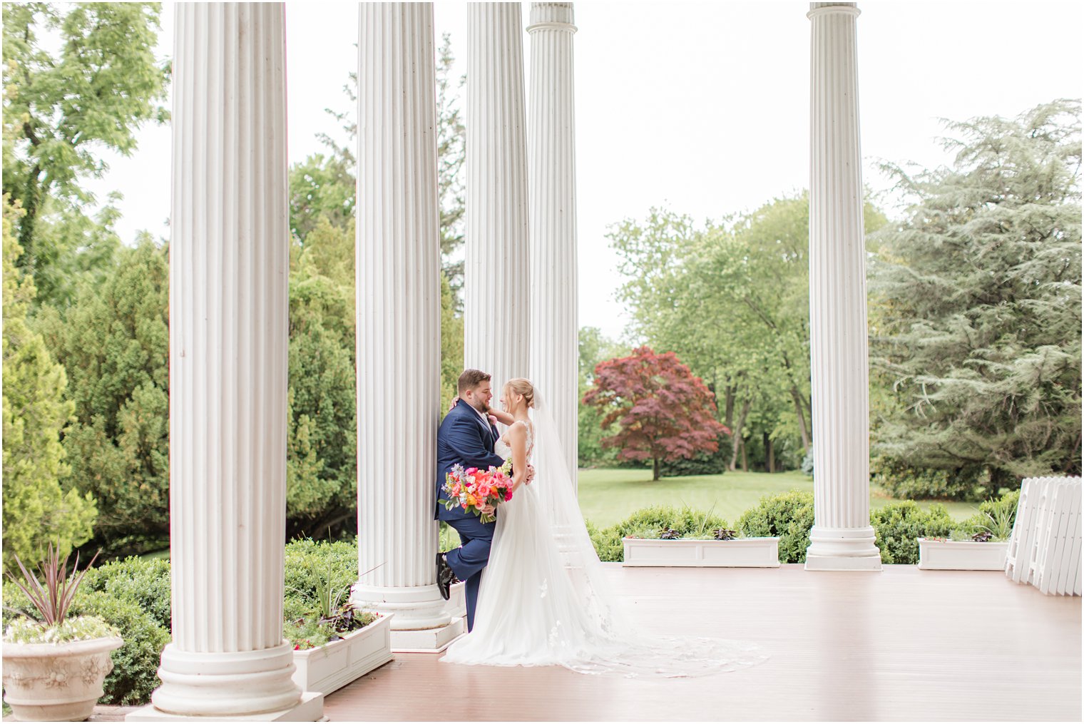 bride leans into groom during spring wedding photos along white pillars at Rosemont Manor