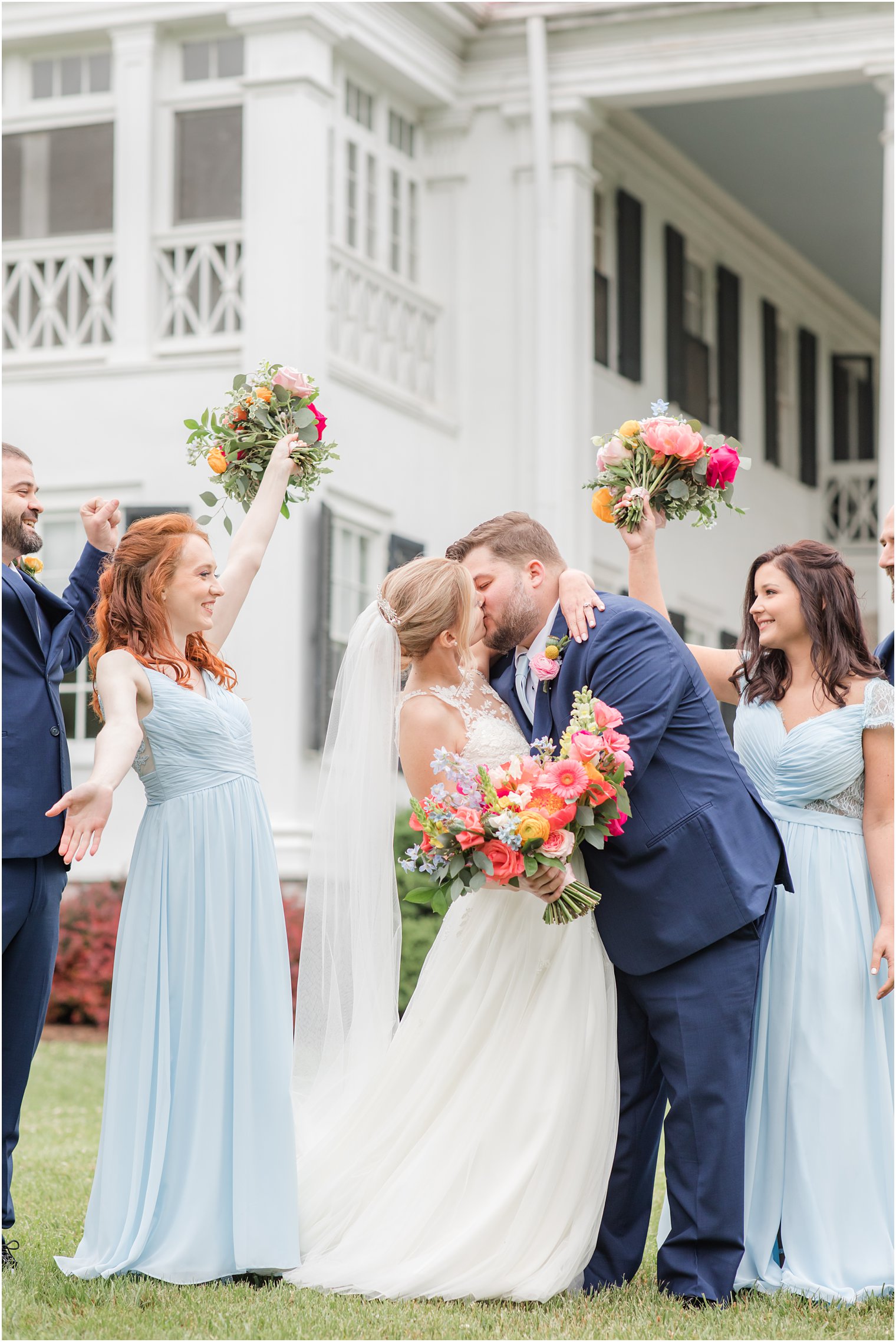 groom kisses bride with bridal party cheering next to them 