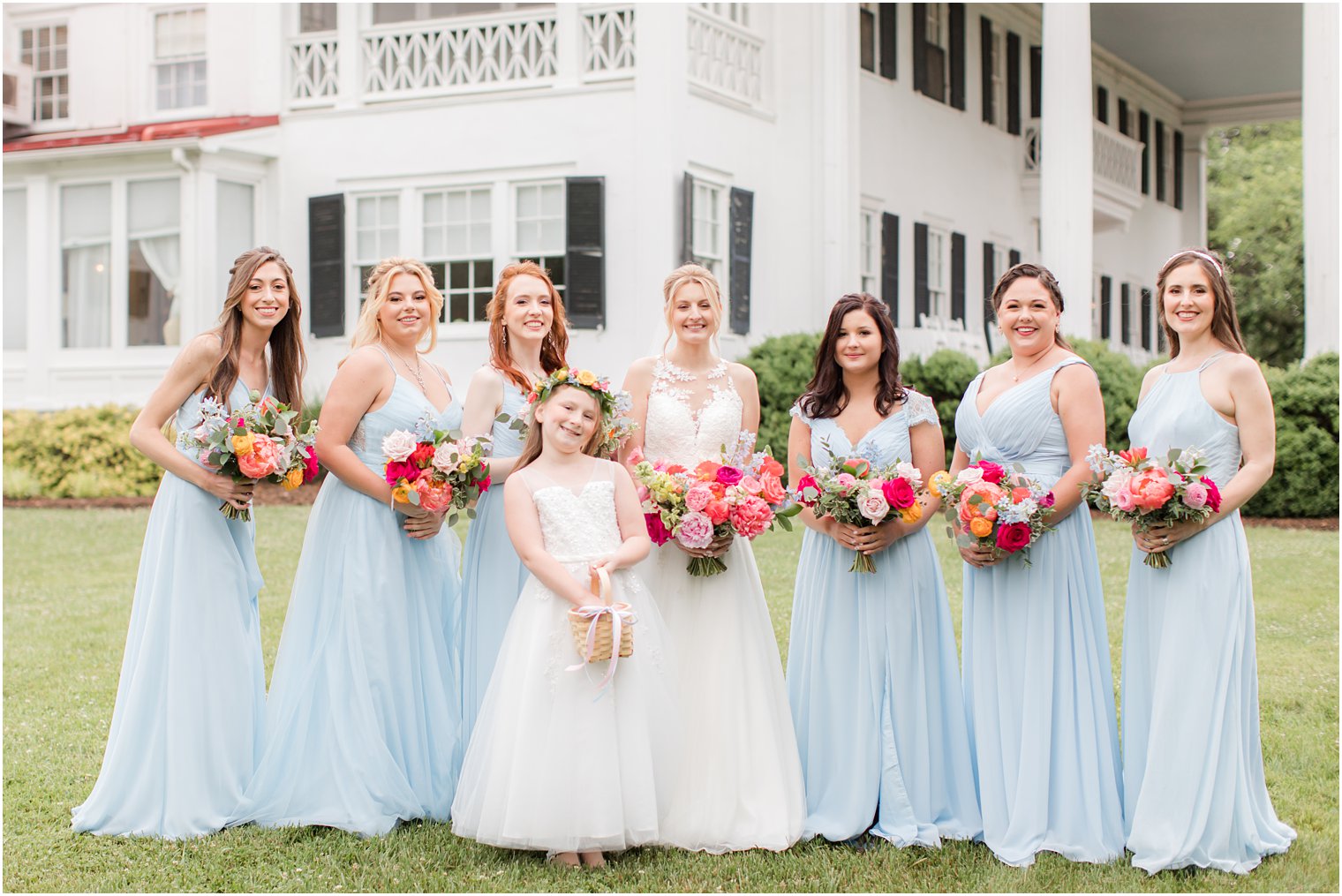 bride poses with bridesmaids in light blue dresses with bright wildflowers bouquets 