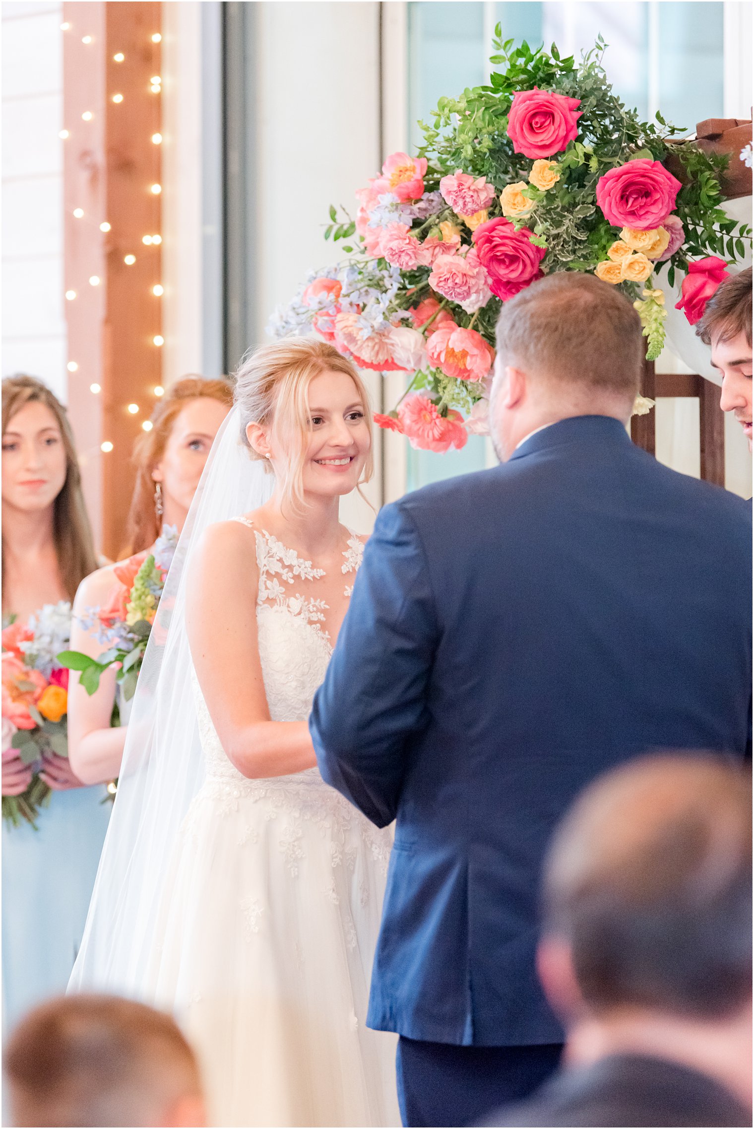 bride looks at groom during wedding ceremony under floral arbor 