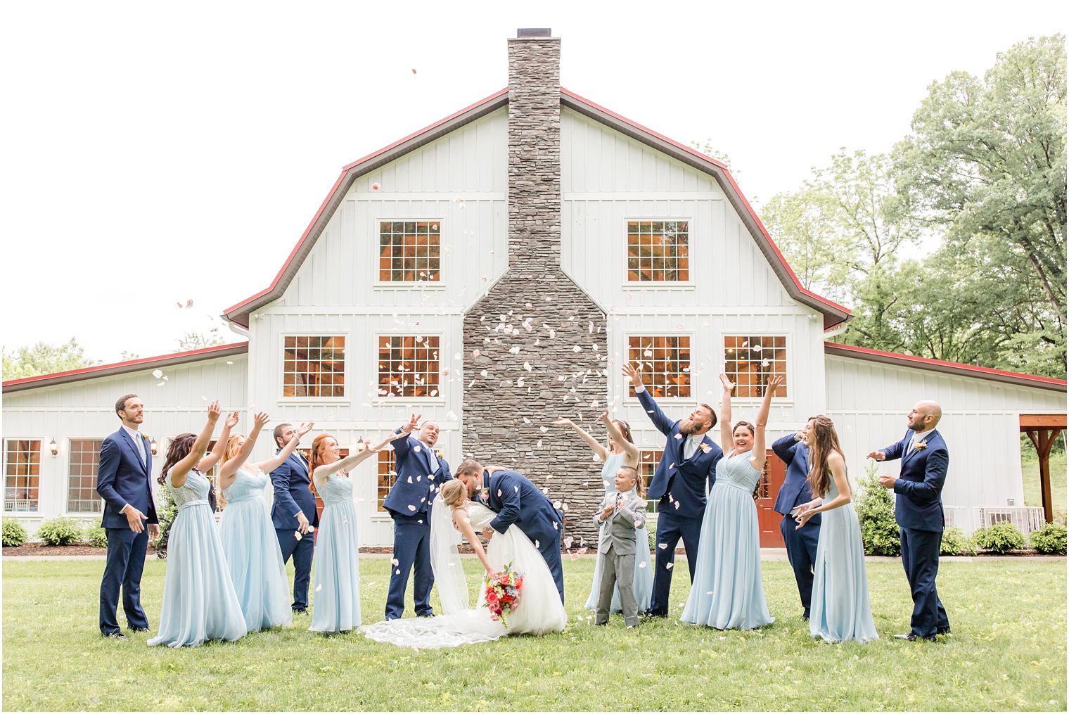 bridal party throws flower petals outside Rosemont Manor while bride and groom kiss