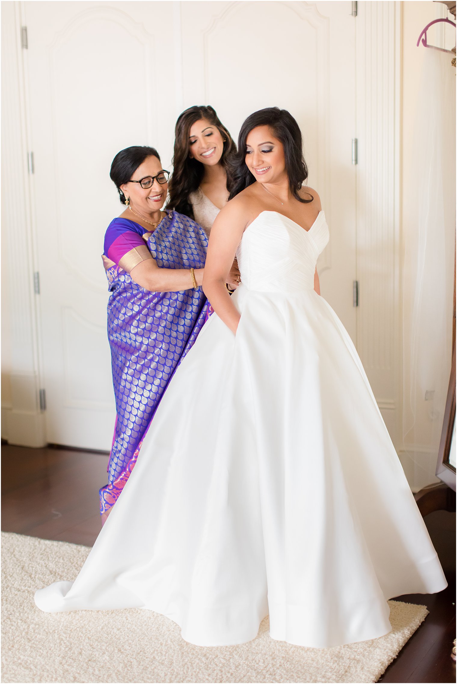 maid of honor and mother help bride with wedding gown