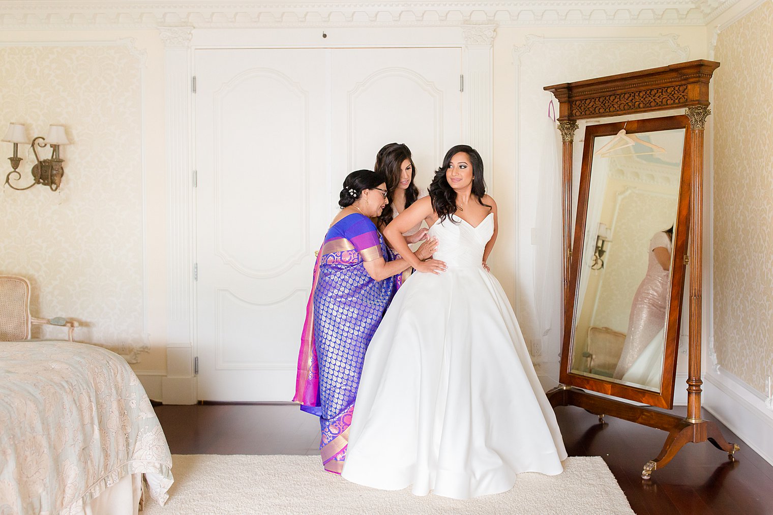 Maid of honor and mother helping bride get dressed