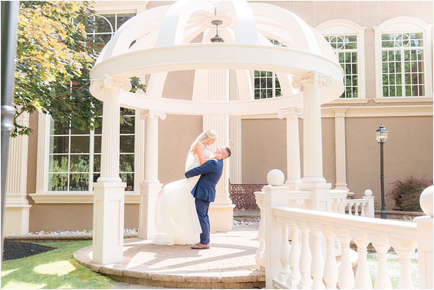 groom lifts bride up in pergola during NJ wedding photos at Brigalias