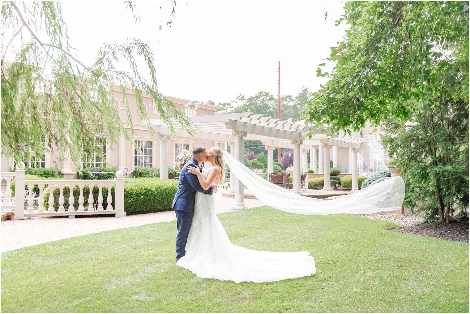 bride and groom kiss by pergola at Brigalias with bride's veil floating behind her 