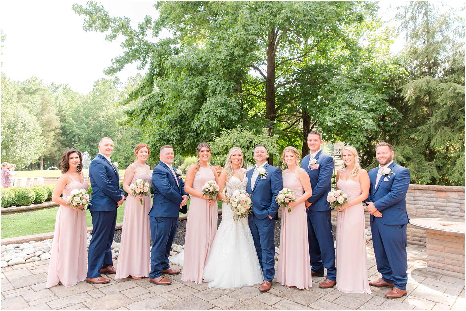 bride and groom pose with wedding party in navy suits and light pink gowns 