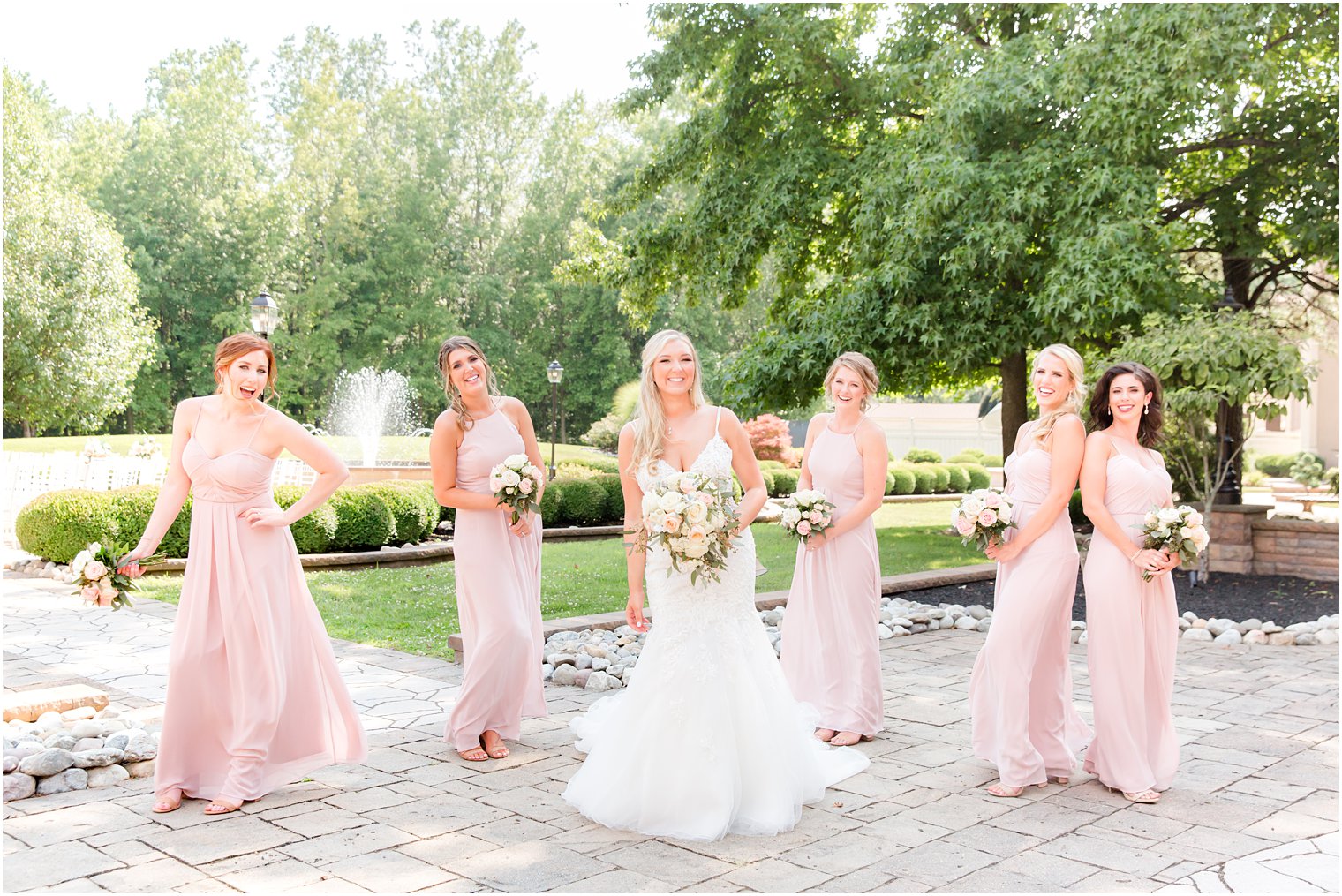bride poses with bridesmaids in light pink gowns before NJ wedding