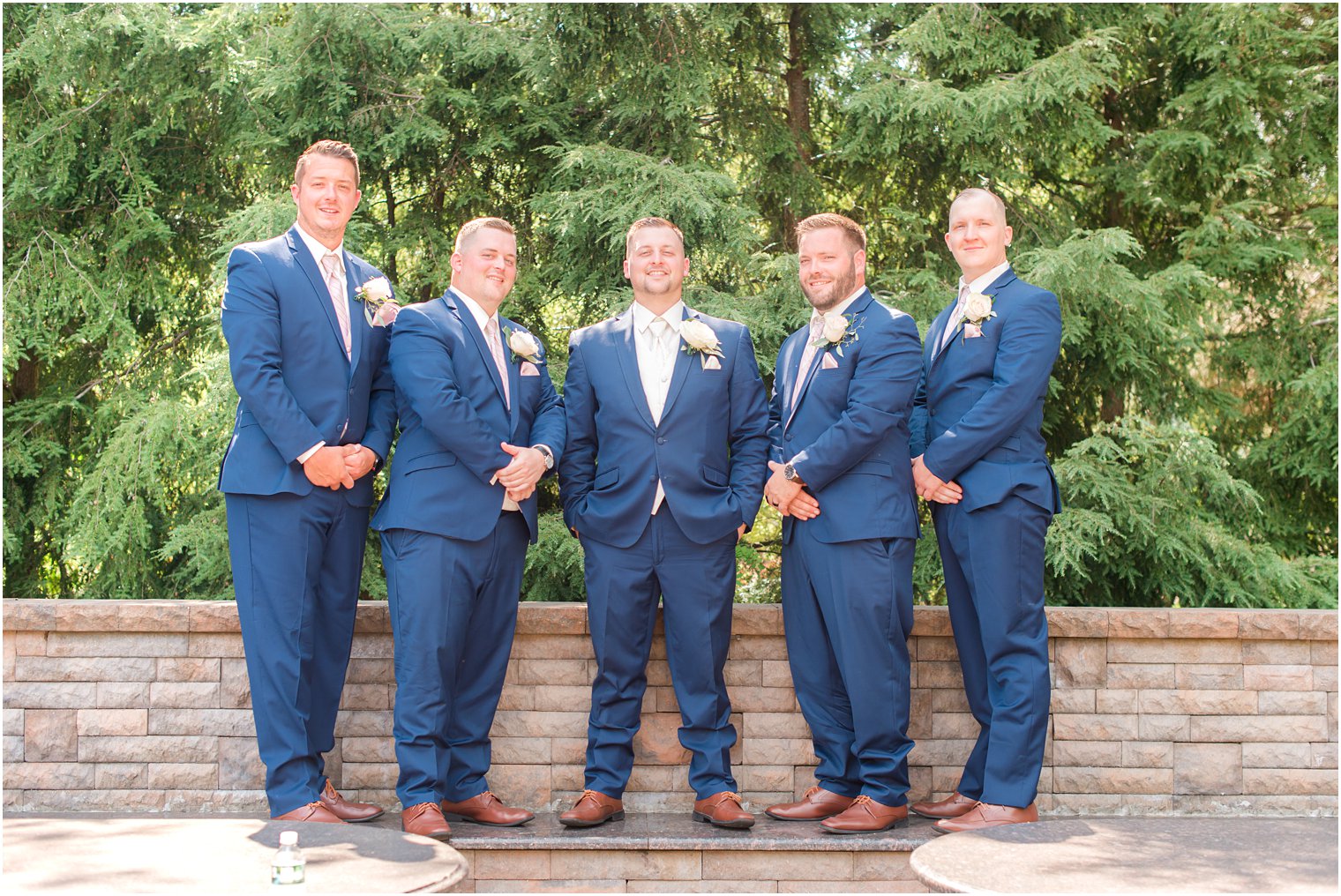 groom and groomsmen in navy suits pose by brick wall in New Jersey 