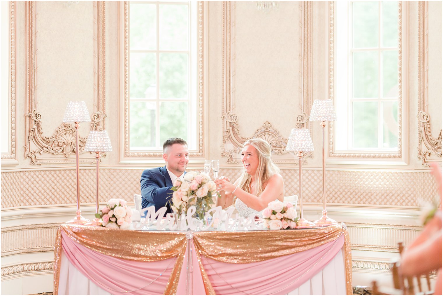 newlyweds toast at sweetheart table with pink and gold decor 