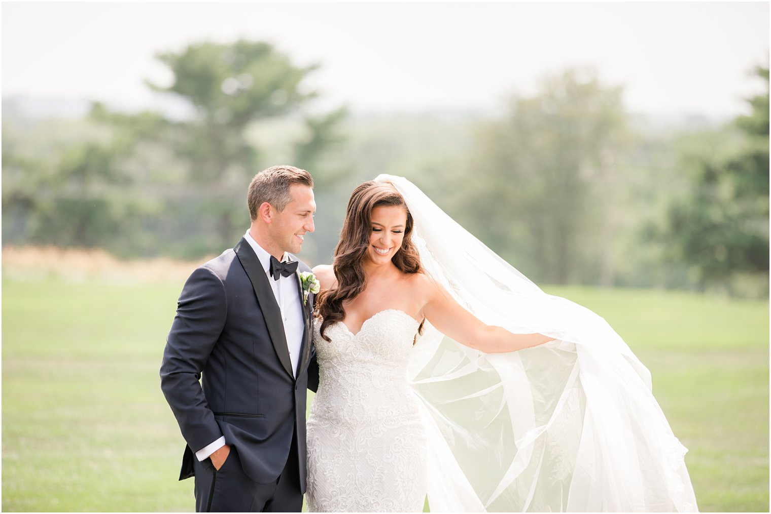 newlyweds laugh while bride lifts veil during wedding photos at Navesink Country Club