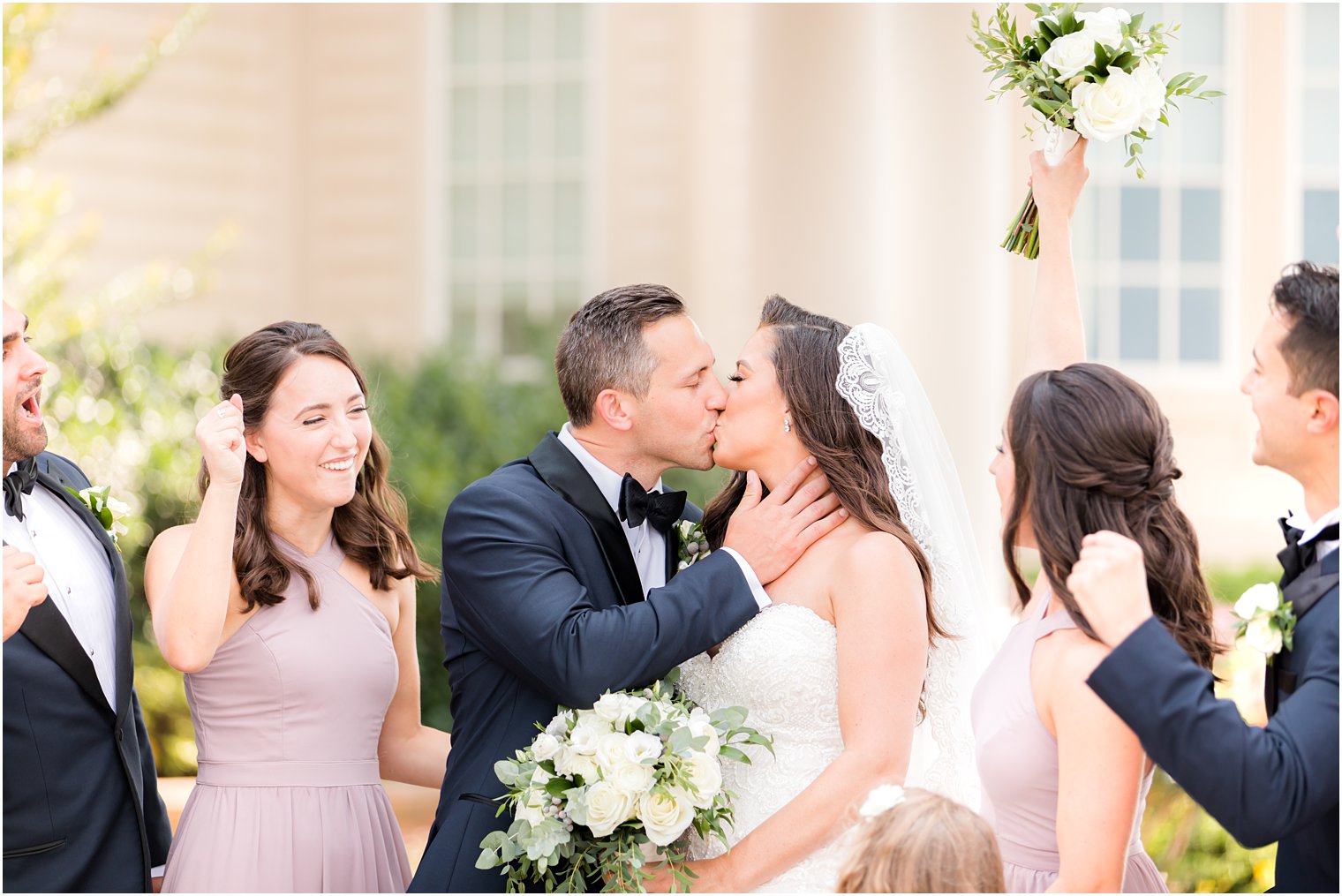 wedding party cheers while bride and groom kiss