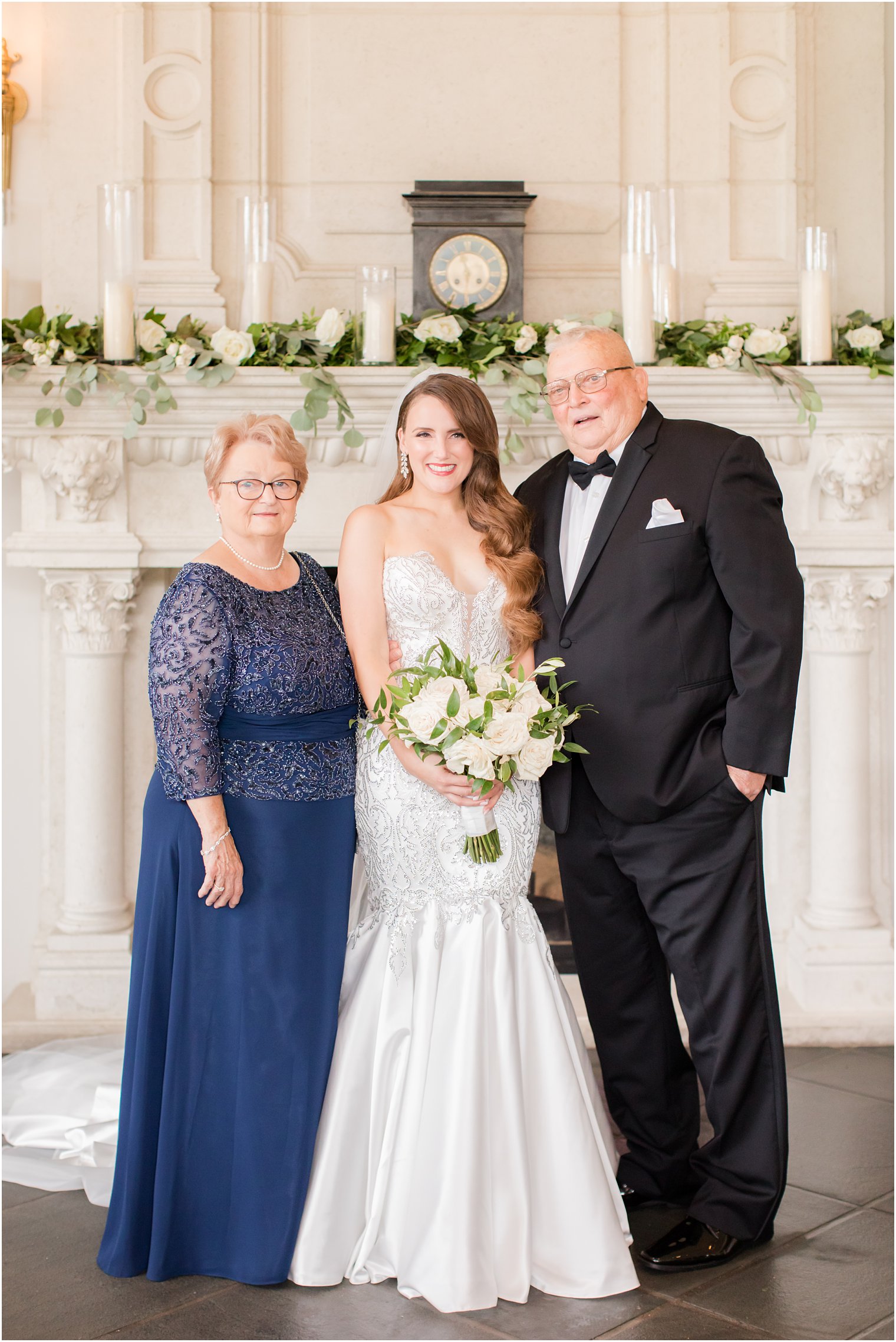 bride poses with parents in front of fireplace at Park Chateau Estate