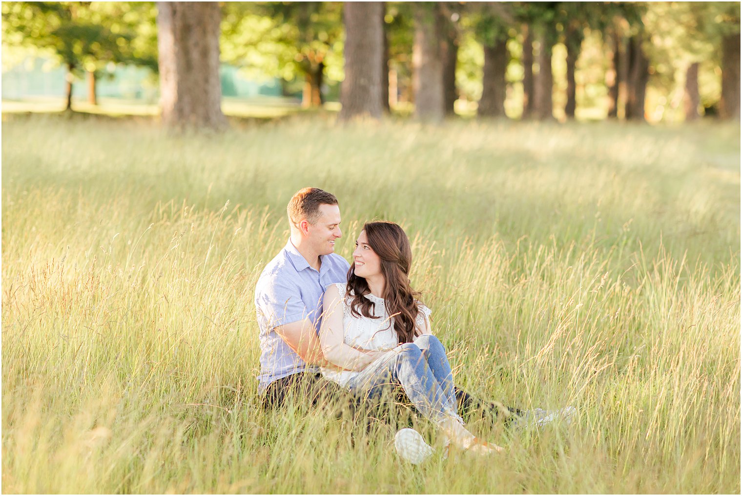 engaged couple sits in the grass during Poconos PA engagement portraits 