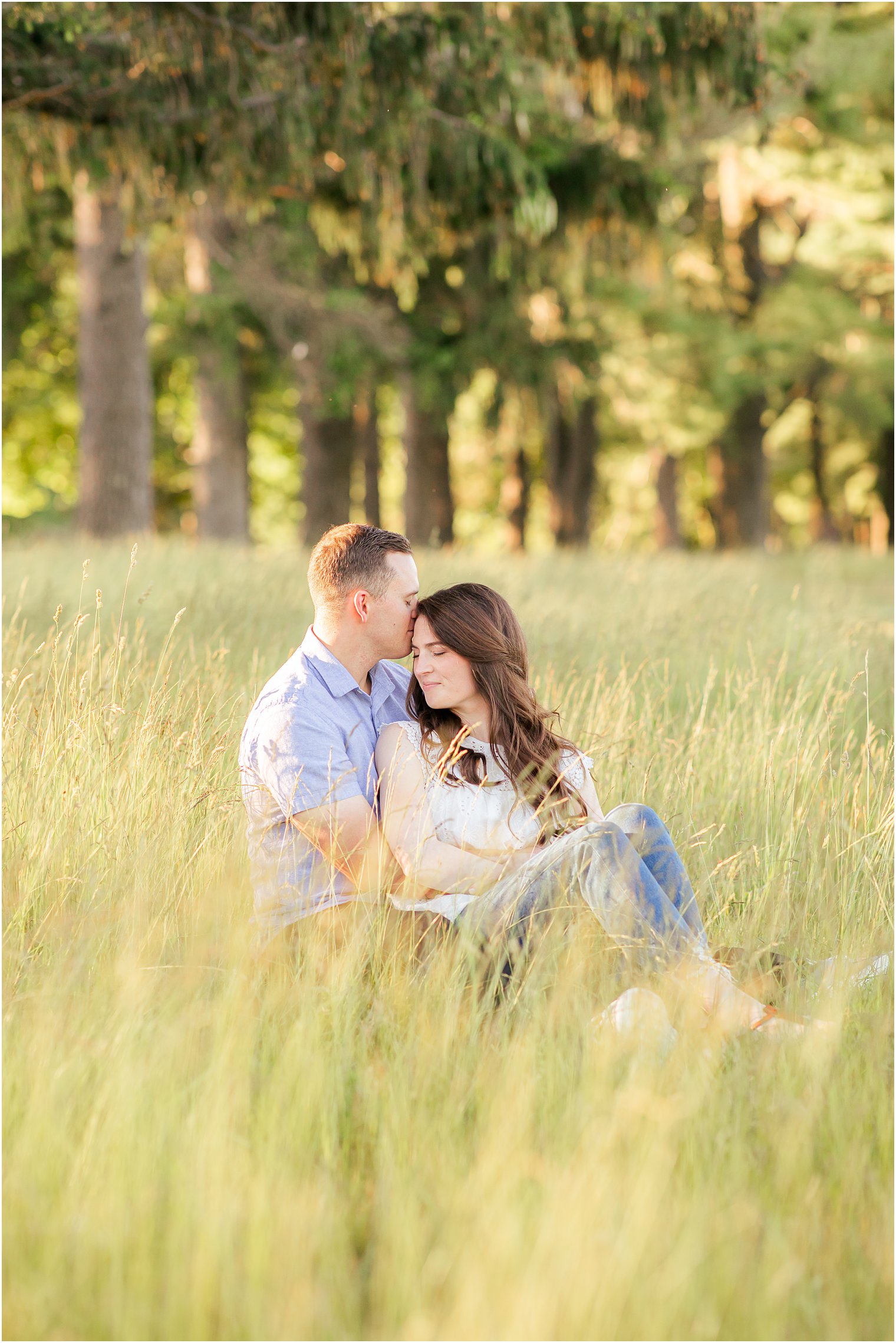 bride and groom sit in tall grass during engagement photos in PA