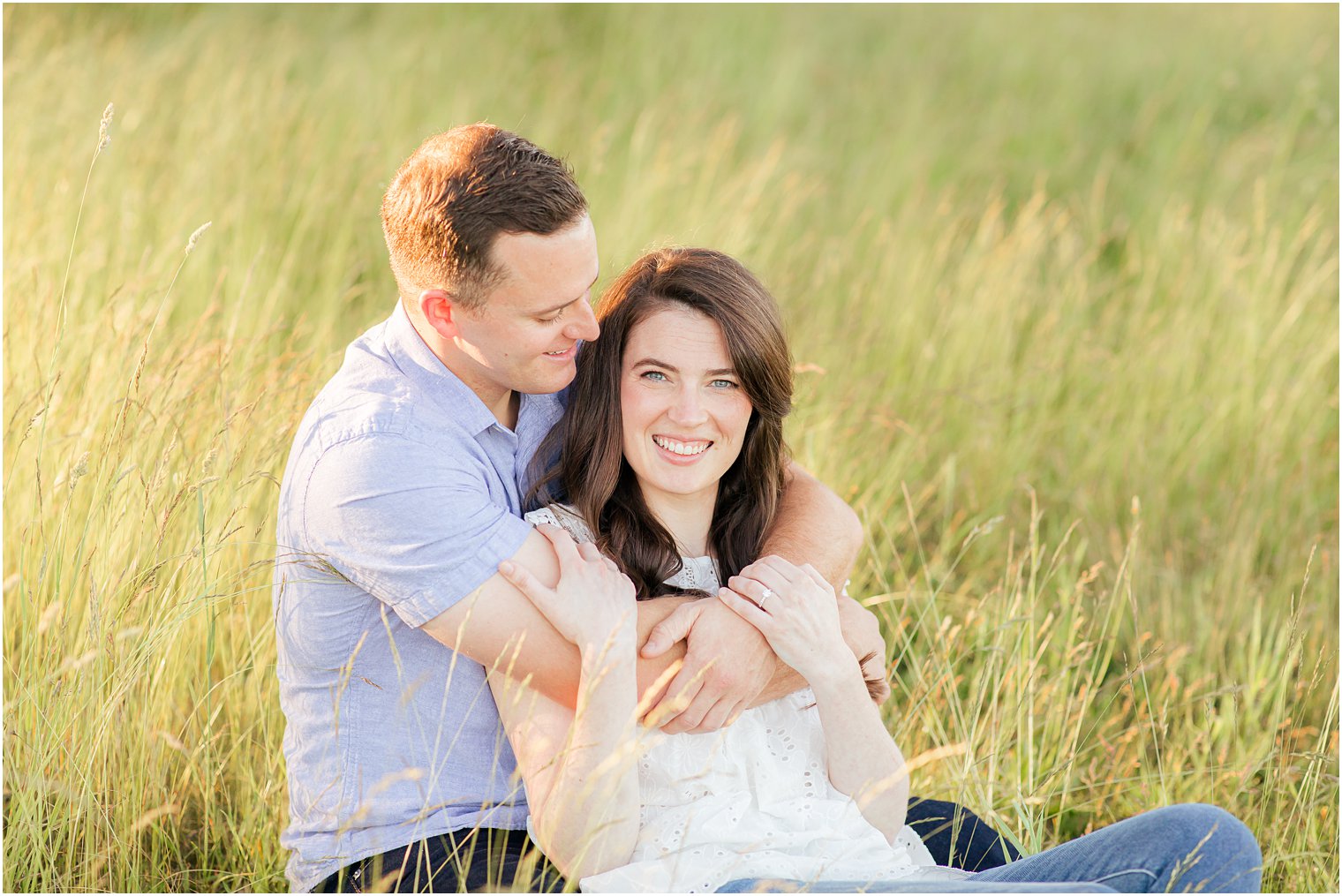 groom holds bride leaning against his chest in the grass during the Poconos PA engagement photos