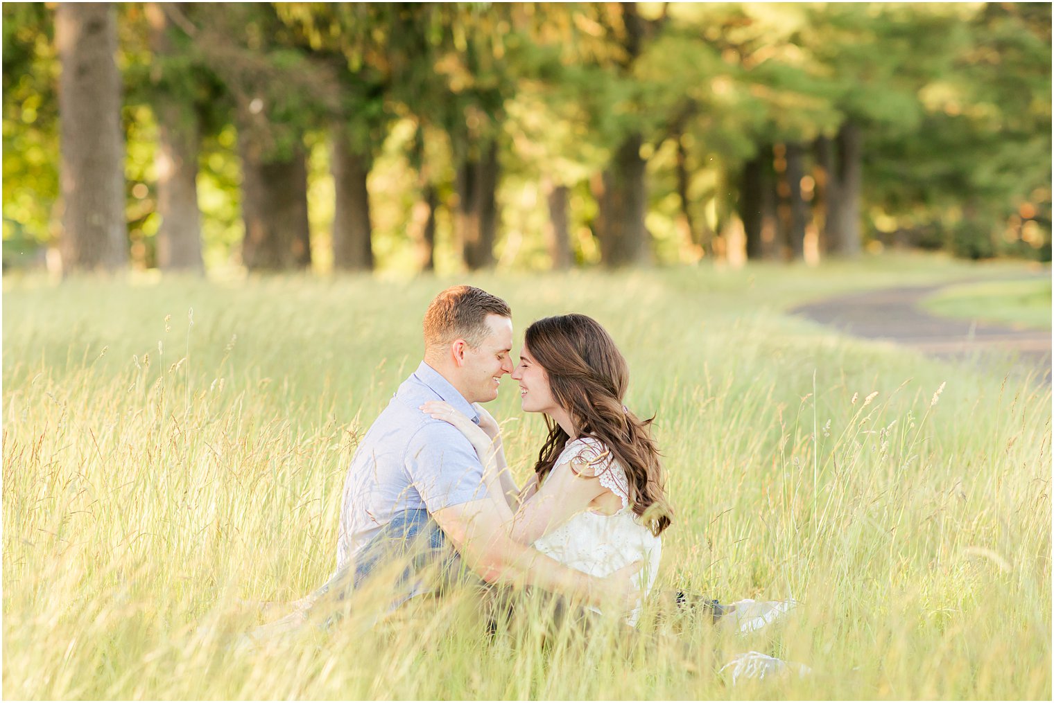 bride and groom sit together laughing in grass during PA engagement photos