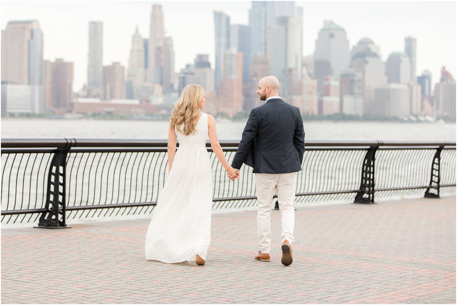 bride and groom hold hands along waterfront for summer Hoboken engagement session